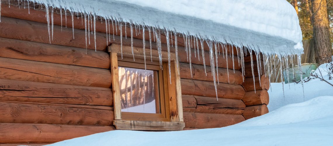 Icicles hanging from the roof of the house. Melting snow on the roof. Dangerous sharp transparent icicles hanging on the roof. Safety